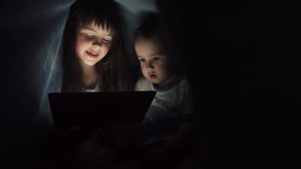 Девочка и мальчик читают книгу под одеялом — стоковое видео