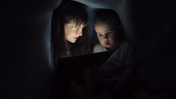 Girl and boy reading book under blanket — Stock Video