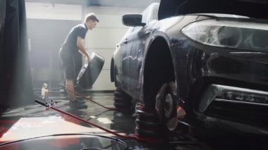 Üniformalı oto tamircisi arabanın tekerini değiştiriyor.