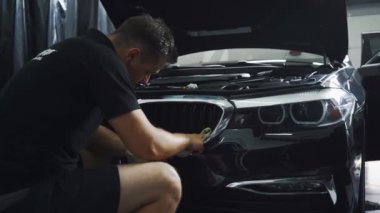 Otomotiv personeli araba tamponunu bezle parçalıyor.