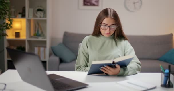 Junge Brünette liest Buch am Tisch — Stockvideo