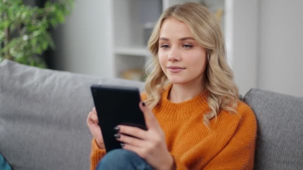 Frau sitzt auf Couch und hält Tablet in der Hand — Stockvideo