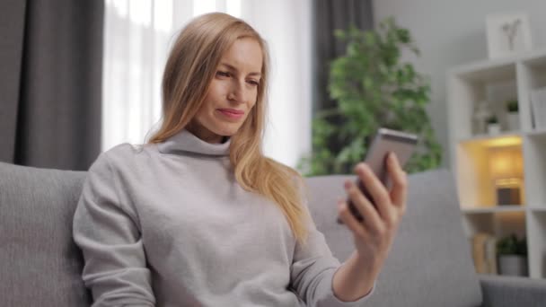 Frau entspannt sich auf Couch und nutzt Smartphone — Stockvideo