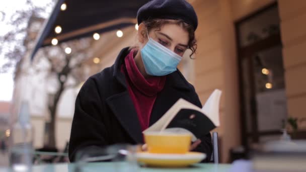 Egy maszkos nő könyvet olvas a kávézóban. — Stock videók