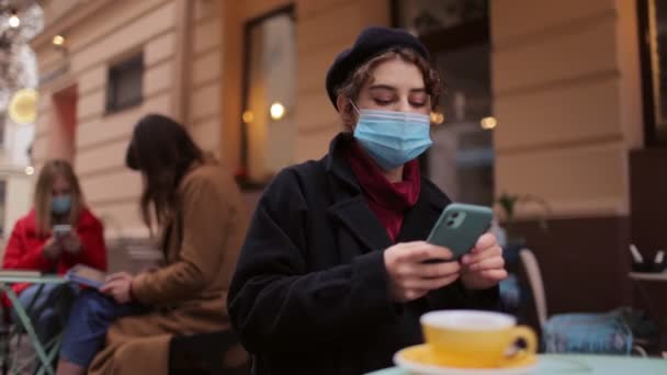 Brünette in Maske mit Smartphone im Café — Stockvideo