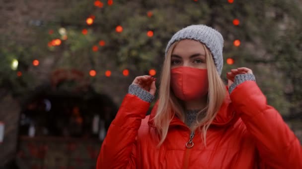 Γυναίκα με κόκκινη μάσκα χαμογελά και κοιτάζει την κάμερα — Αρχείο Βίντεο