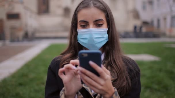 Brünette in Maske mit Smartphone im Freien — Stockvideo