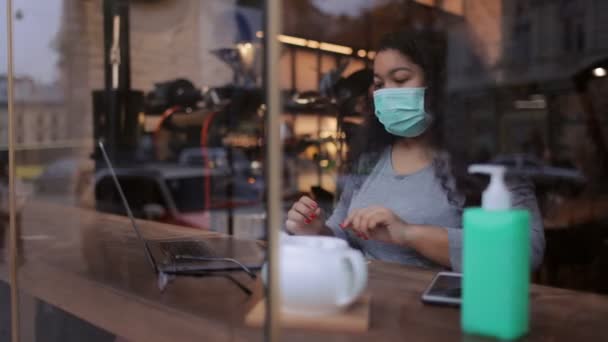 Γυναίκα με μάσκα που δουλεύει σε λάπτοπ στο καφέ. — Αρχείο Βίντεο