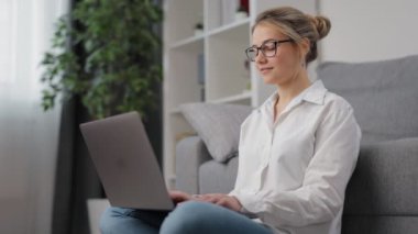 Sarışın yerde oturuyor ve dizüstü bilgisayar kullanıyor.