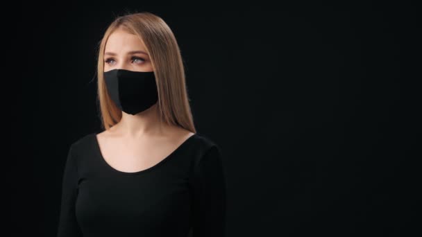 Kobieta w masce medycznej stojąca na czarnym tle — Wideo stockowe