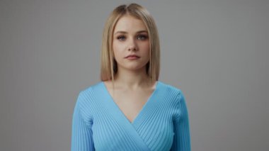 Mavi kazaklı ciddi bir kadın stüdyoda poz veriyor.