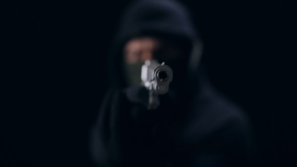 Убийца в маске держит пистолет на черном фоне — стоковое видео