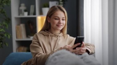 Kanepede elinde akıllı telefonla dinlenen bir kadın.