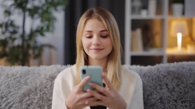 Sarışın kanepede dinleniyor ve akıllı telefon kullanıyor.