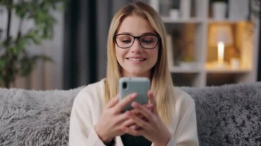 Sarışın, akıllı telefonlu kanepede dinleniyor.