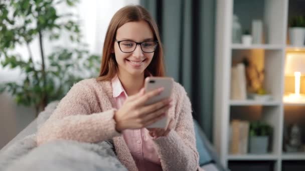 Frau in Brille mit Smartphone auf Couch — Stockvideo