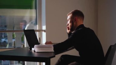 Telefonla konuşan ve ofiste dizüstü bilgisayarda çalışan bir adam.