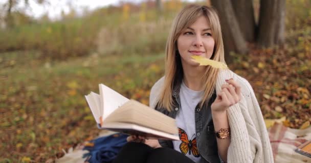 Drömmande blond läsning bok i höstparken — Stockvideo