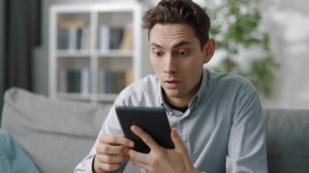 Překvapený muž při pohledu na obrazovku tabletu doma — Stock video