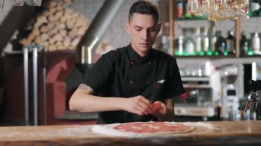 Şef pizza tabanına sosis dilimleri koyuyor.