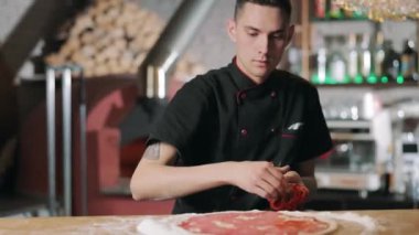 Şef pizza tabanına kırmızı biber koyuyor.