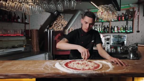 Chef aggiungendo formaggio grattugiato sulla base della pizza — Video Stock