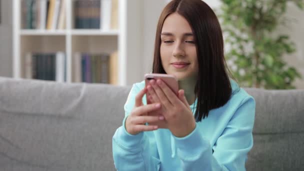 Lächelnde Frau sitzt mit Smartphone auf Sofa — Stockvideo