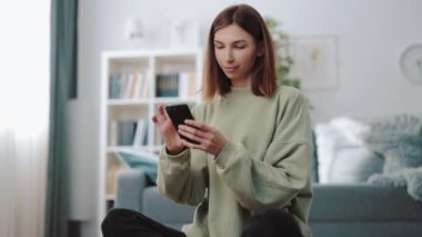 Kadın akıllı telefonuyla evde dinleniyor.