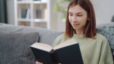 Kanepede dinlenirken kitap okuyan bir kadın.