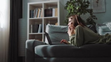 Kanepede yatarken dizüstü bilgisayar kullanan kadın.