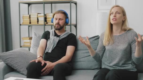 Egy férfi a fülhallgatóban nem vesz tudomást a feleségéről. — Stock videók