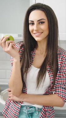 Neşeli bir insan parlak bir mutfakta elinde yeşil bir elmayla duruyor. Atmosfer davetkar ve sıcak. Sağlıklı yemek ve güzel yemeklere olan sevgisini gösteriyor..