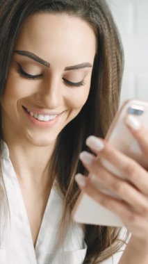 Bir kadın, akıllı telefonunu kontrol ederken mutfaktan taze bir salata hazırlıyor. Gülümsüyor, günlük rutininde gündelik ama çekici bir an sergiliyor..