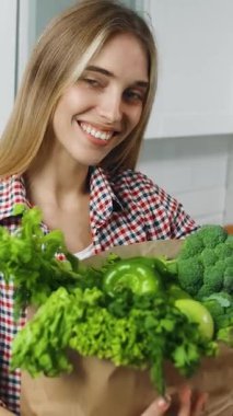 Bir kadın elinde taze sebzelerle dolu bir çanta tutarken gülümsüyor. Canlı ürün seçimiyle besleyici yemekler hazırlamaya hazır..