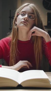 Kitap okurken derin düşüncelere dalmış bir kadın evde oturuyor. Sıcacık bir ışık ve yansımayı ve odaklanmayı teşvik eden sakin bir atmosferle ortam rahat..