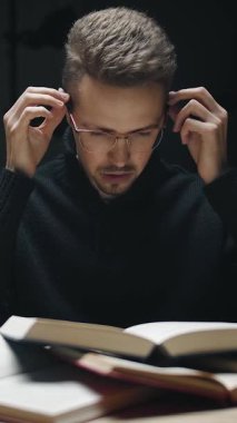 Gece geç saatlerde kitap okumaya odaklanmış bir adam masada oturuyor. Gözlüklerini diğer kitaplarla çevrili olarak ayarlıyor. Atmosfer sakin ve sessiz. Çalışmak için mükemmel..