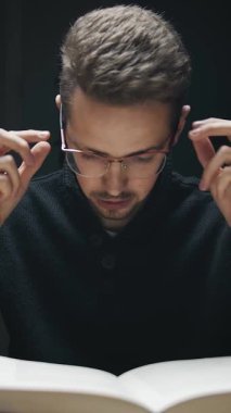 Geceleri kitap okumaya dalmış bir adam sessizce oturur. Konsantrasyonu, huzurlu bir keşif ve bilgi anını vurguluyor. Loş ışık, sakin atmosfere katkı sağlıyor..