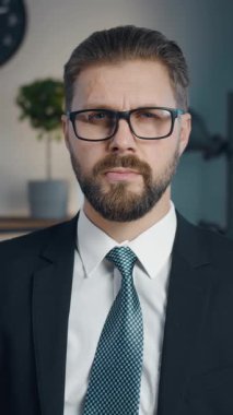 Resmi giyinmiş bir işadamı modern ofisinde otururken sıcak bir şekilde gülümser. Atmosfer profesyonelce, önemli bir toplantı sırasında odak ve arkadaşlığın bir karışımını gösteriyor..