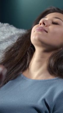 Bir kadın kanepede rahat bir şekilde yatarak evde vakit geçirmekten zevk alır. Huzurlu bir durumda, rahatlıyor ve yaşam alanının rahatlığında dinleniyor..