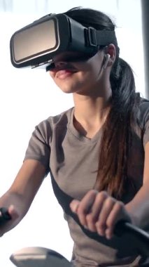 Bir insan evdeki egzersiz bisikletinde sanal gerçeklik kulaklığı kullanarak sağlık ve eğlenceye odaklanmış bir fitness seansına katılır..