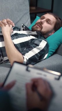 Bir adam psikolog seansı sırasında duygularını tartışırken kanepede dinlenir. Odak noktası duygusal keşifler ve içgörü..