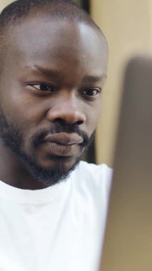 Bir kişi masa başında çalışırken siyah bir dizüstü bilgisayar arızası yaşar, bu da hayal kırıklığı ve kafa karışıklığına yol açar..