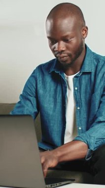 Bir adam dizüstü bilgisayarını kullanarak koltuğunda oturuyor, evde işine odaklanmış ve meşgul..