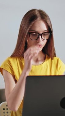 Gözlüklü bir kadın laptopuyla çalışırken gülümsüyor ve ev ortamında işine odaklanıyor..