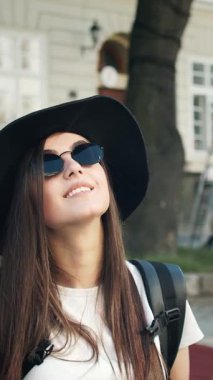 Turist gülümser ve güneş gözlüğü ve şapka takarken açık havada fotoğraf için poz verir..