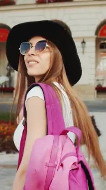 Parlak bir alanda şık bir şapka ve güneş gözlüğü takmış gezen bir insan manzaranın ve seslerin tadını çıkarır..