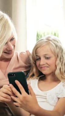 Bir kız ve annesi rahat oturma odalarında akıllı telefona bakmaktan hoşlanırlar..