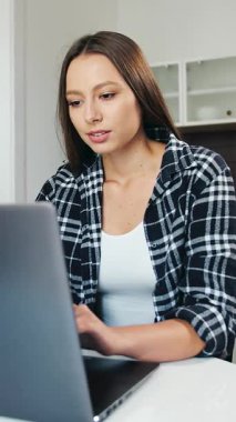 Evde çalışırken bilgisayarına odaklanan bir kadın görevinin keyfini çıkarıyor ve ekranda gülümsüyor.