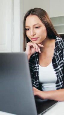 Bir kadın evinde rahat bir ortamda çalışırken dizüstü bilgisayarına odaklanır ve verimliliğini gösterir.