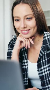 Bir kadın, açık ve rahat bir mekanda çalışırken dizüstü bilgisayarına odaklanır.